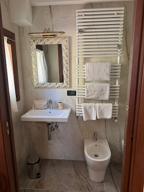 A bathroom with a marble wall, a sink, a bidet, a towel rack, and a mirror with a gold frame. - Ca Pierre (Venice)