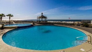 A large, clear blue pool with a gazebo and lounge chairs, surrounded by a deck and palm trees, overlooking the ocean. - Summer House Condo 503B (Orange Beach)