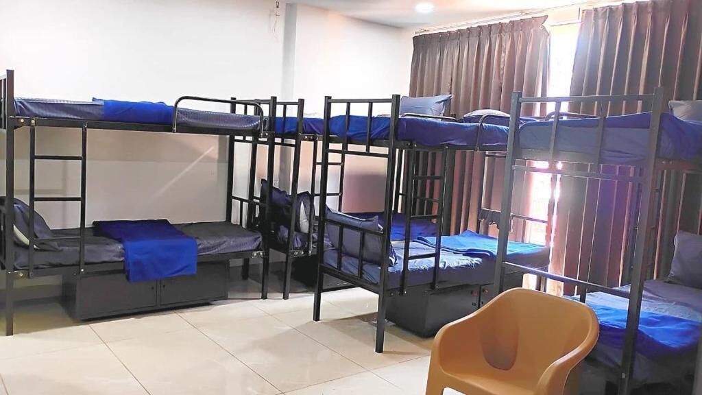 A dormitory room with bunk beds, a chair, and a window with curtains.