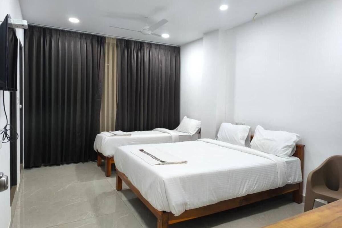 Una habitación de hotel con dos camas individuales, cabecera de madera, televisor de pantalla plana, ventilador de techo y una mesa.