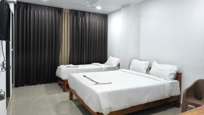 Habitación de hotel con dos camas individuales, cabecero de madera, televisor de pantalla plana, ventilador de techo y una mesa.
