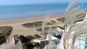 A beach view from a hotel balcony with a clear sky, sandy beach, and parked cars. - SUPERB T4 SEAFRONT WITH ROOFTOP IN ST JEAN DE MONTS (Saint-Jean-de-Monts)