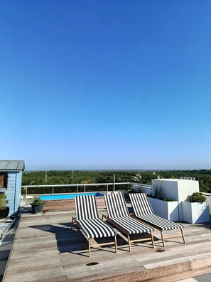 Une terrasse sur le toit, dotée de chaises longues, d’une piscine et offrant une vue sur la ville et la forêt.