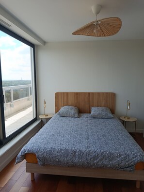 Une chambre moderne avec un grand lit, un ventilateur de plafond et une vue dégagée sur l’extérieur grâce à une grande fenêtre.