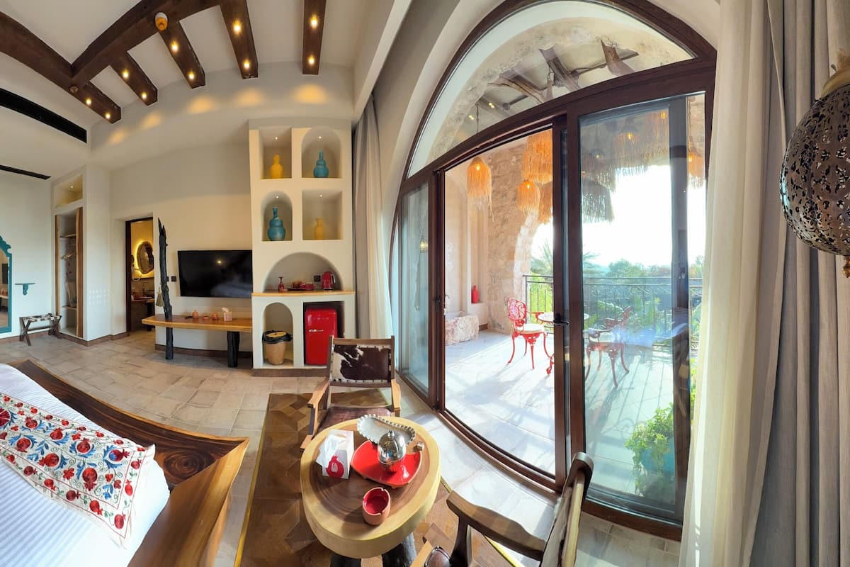Un dormitorio amplio con una cama grande, televisión y balcón con mobiliario exterior.