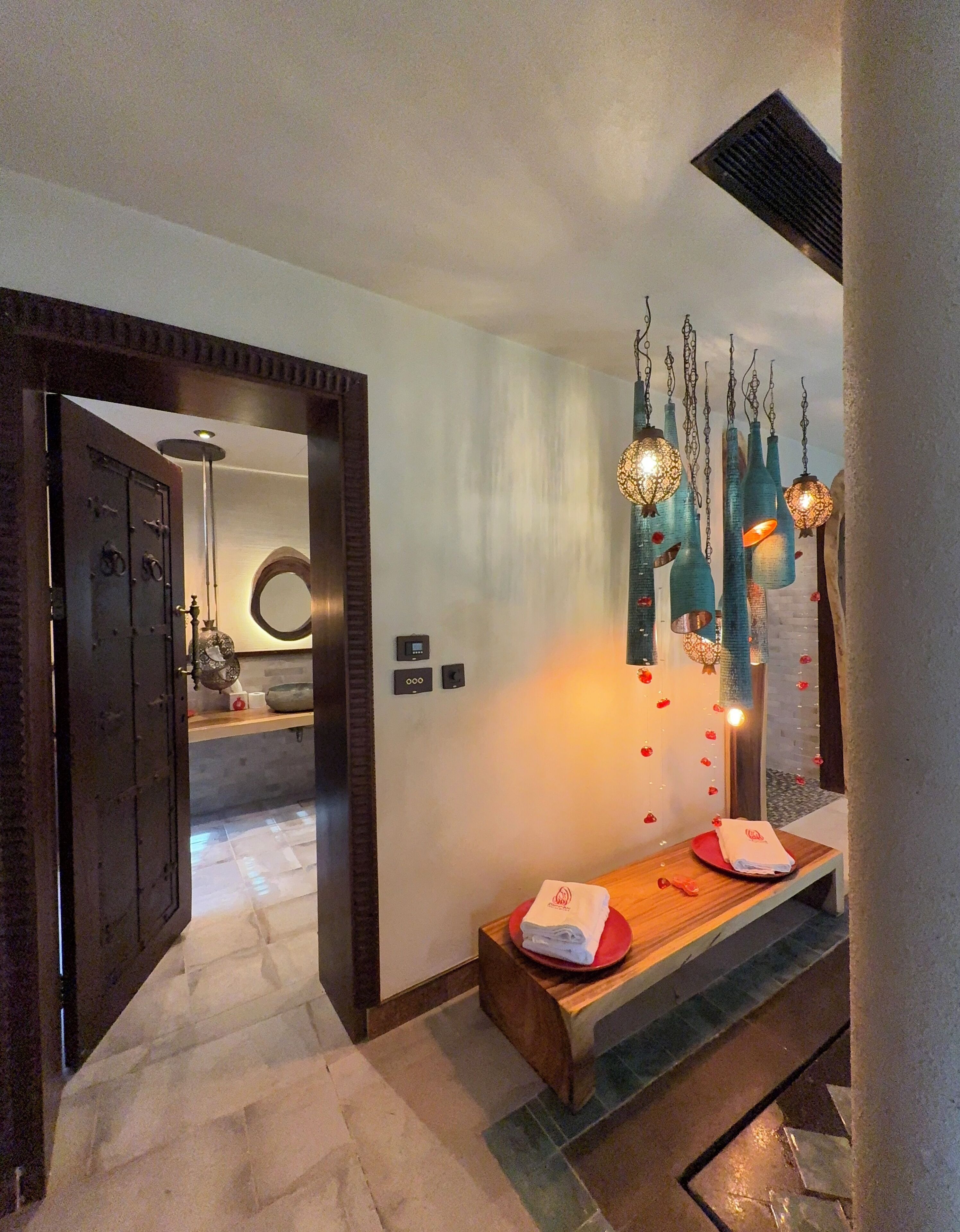 Un hall de hotel con un banco de madera, una lámpara fijada a la pared y una puerta que da a otra habitación.