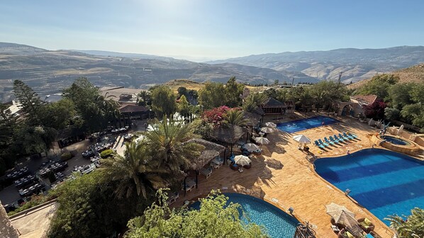 A resort with multiple swimming pools, outdoor seating areas, and a view of distant hills.