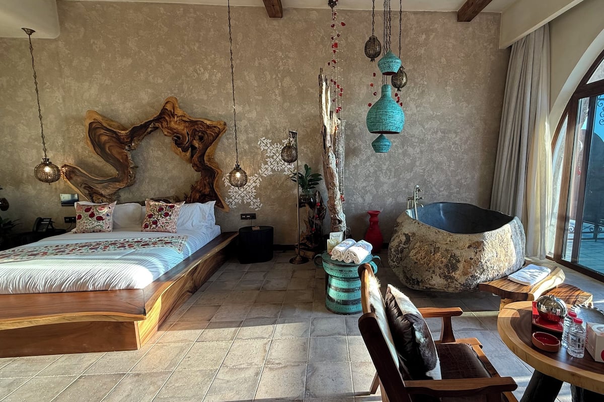 Un dormitorio con una cama grande, una bañera, una mesa de comedor con sillas y vistas al mar a través de amplios ventanales.