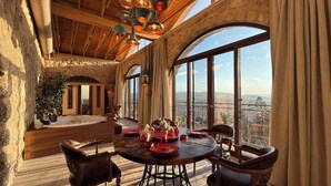 A spacious room with a large dining table, wooden chairs, and a view of the landscape through large windows.