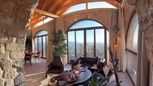 A spacious room with a high ceiling, stone walls, and large arched windows offering a view of the mountains.
