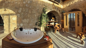 A spa area with a large bathtub, stone walls, and a view of the landscape.
