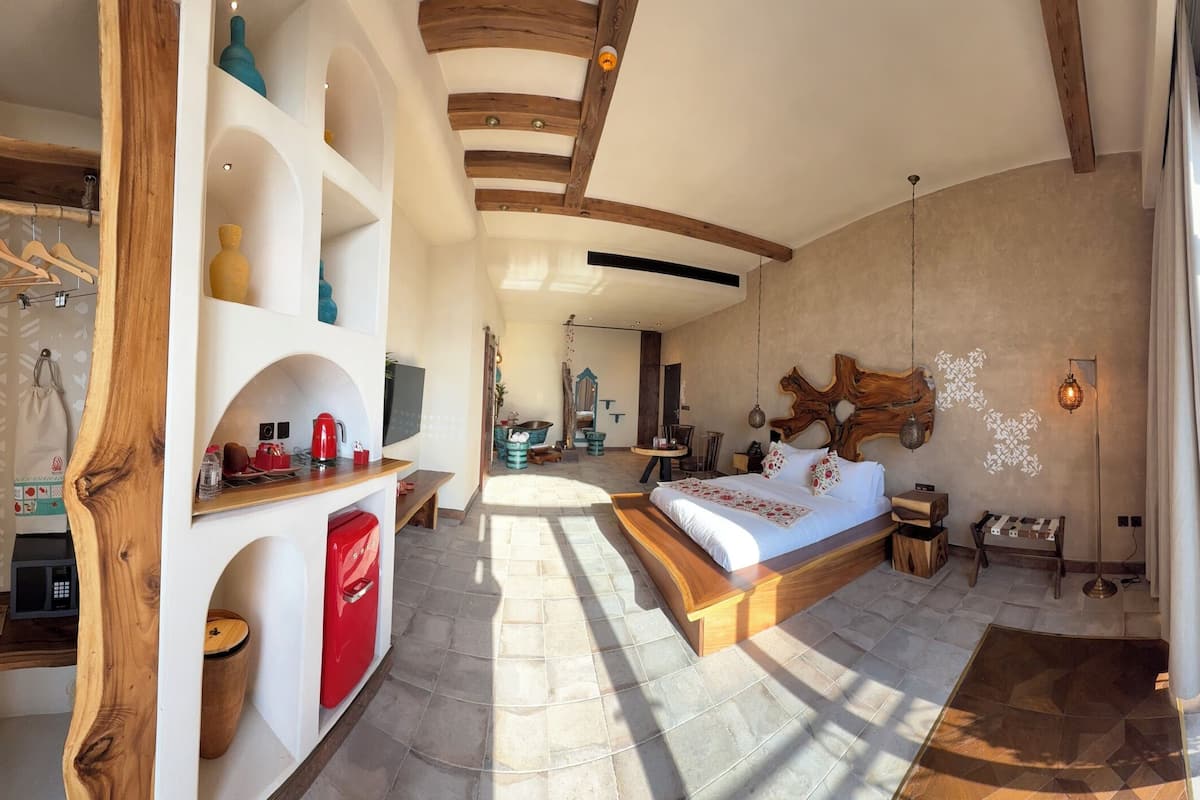 Un dormitorio espacioso con una cama grande, un escritorio de madera y vistas a una piscina y montañas.