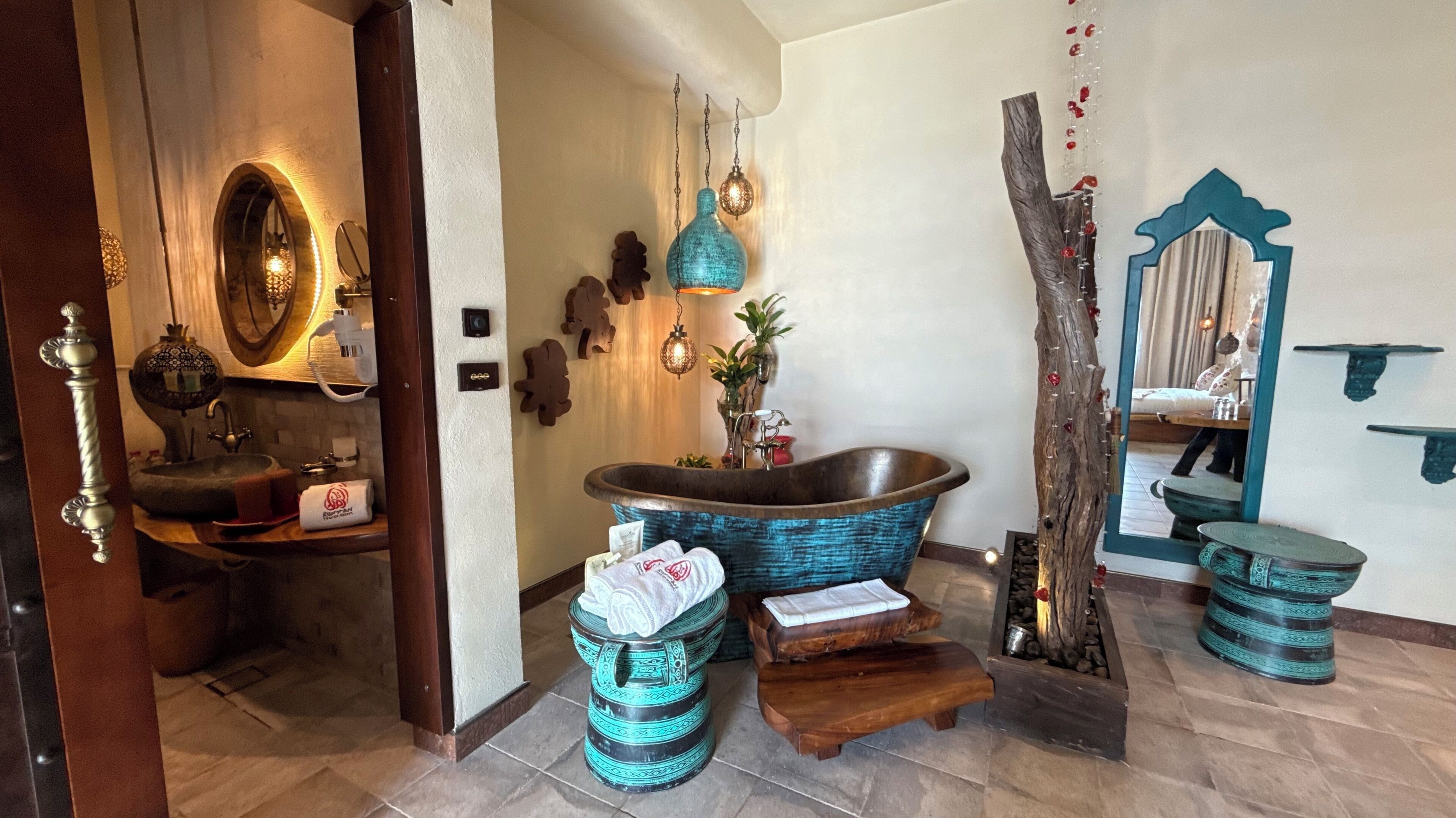 Un baño con una bañera independiente, taburetes de madera y un espejo con marco decorativo.