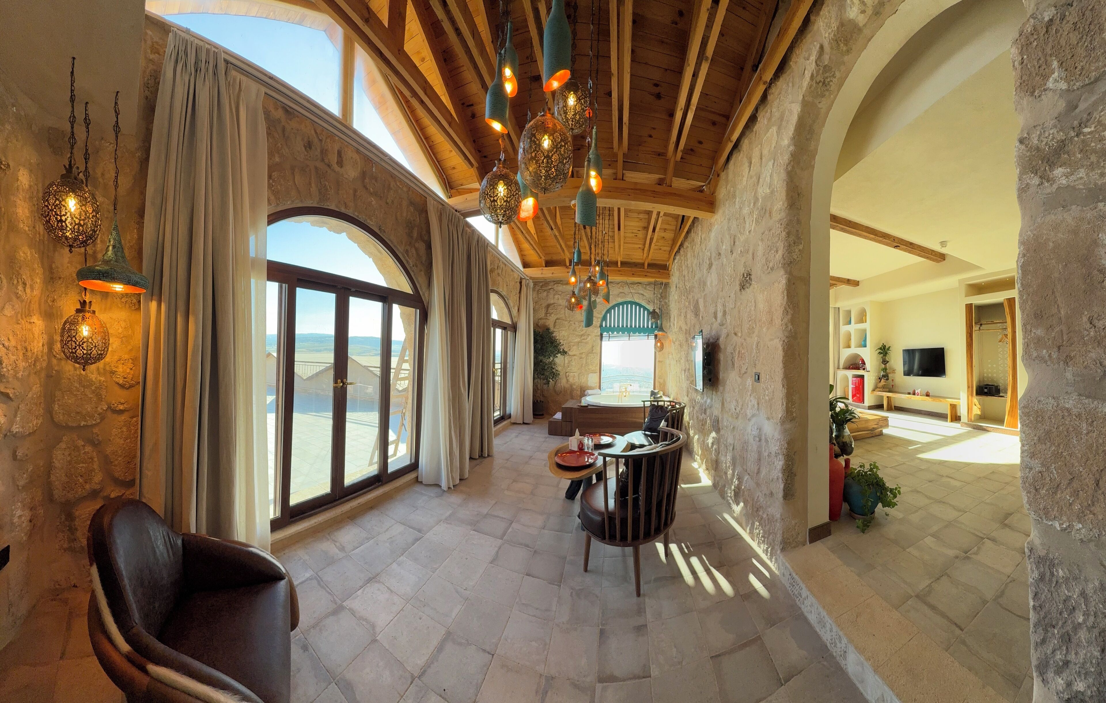 A spacious interior with stone walls, large arched windows, and hanging decorative lights.