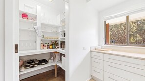 A kitchen with white cabinetry, a window with a view of trees, and various kitchen items on shelves.