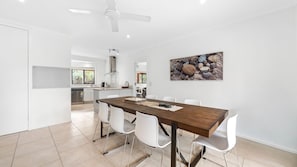 A modern kitchen with white cabinetry, a dining area with a wooden table and white chairs, and a ceiling fan.