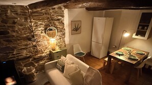 Un salon chaleureux avec un mur en pierre, un canapé blanc, une table à manger dressée pour quatre personnes et un réfrigérateur blanc.