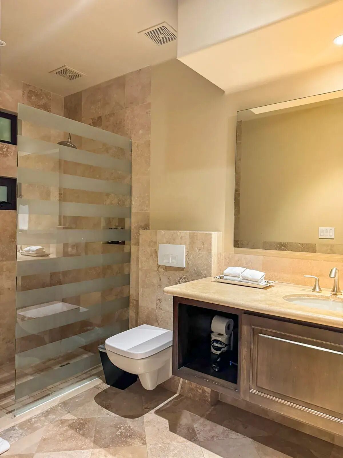 A modern bathroom with a glass shower enclosure, a large mirror, and a vanity with a sink.