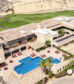 Een resort met een zwembad, terras en een golfbaan op de achtergrond.