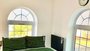Ein Zimmer mit einem Bett, zwei Fenstern, einer Wanduhr und einem Fernseher.