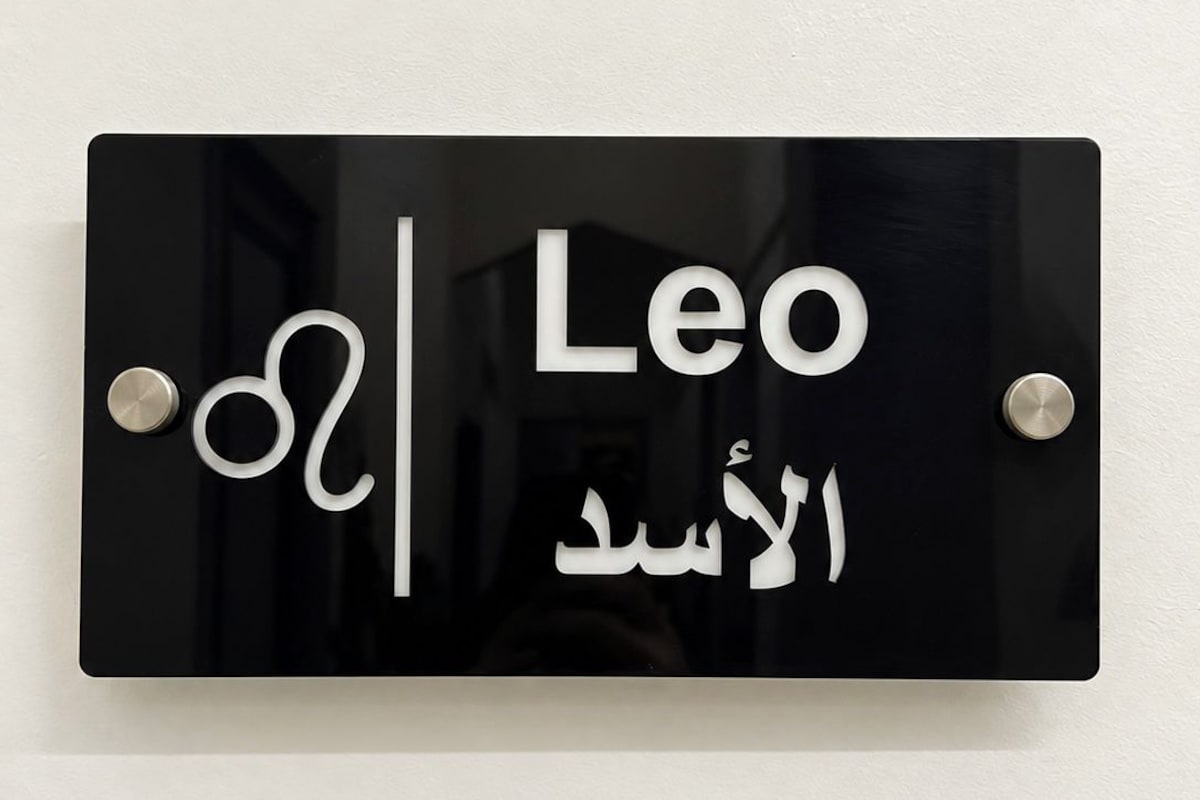 A black sign with white text and Arabic script, mounted on a wall.