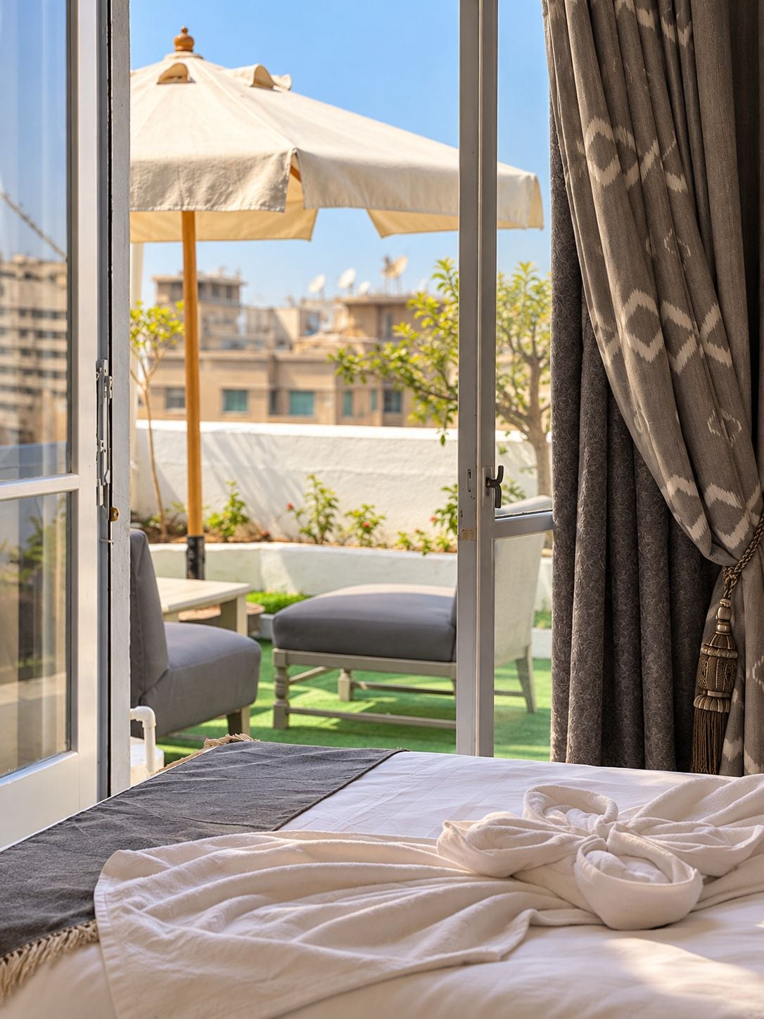 Una camera d'albergo con un letto, vista su una zona relax all'aperto e un balcone con vista sugli edifici.