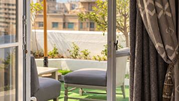 Una camera d'albergo con un letto, vista su una zona relax all'aperto e un balcone con vista sugli edifici.
