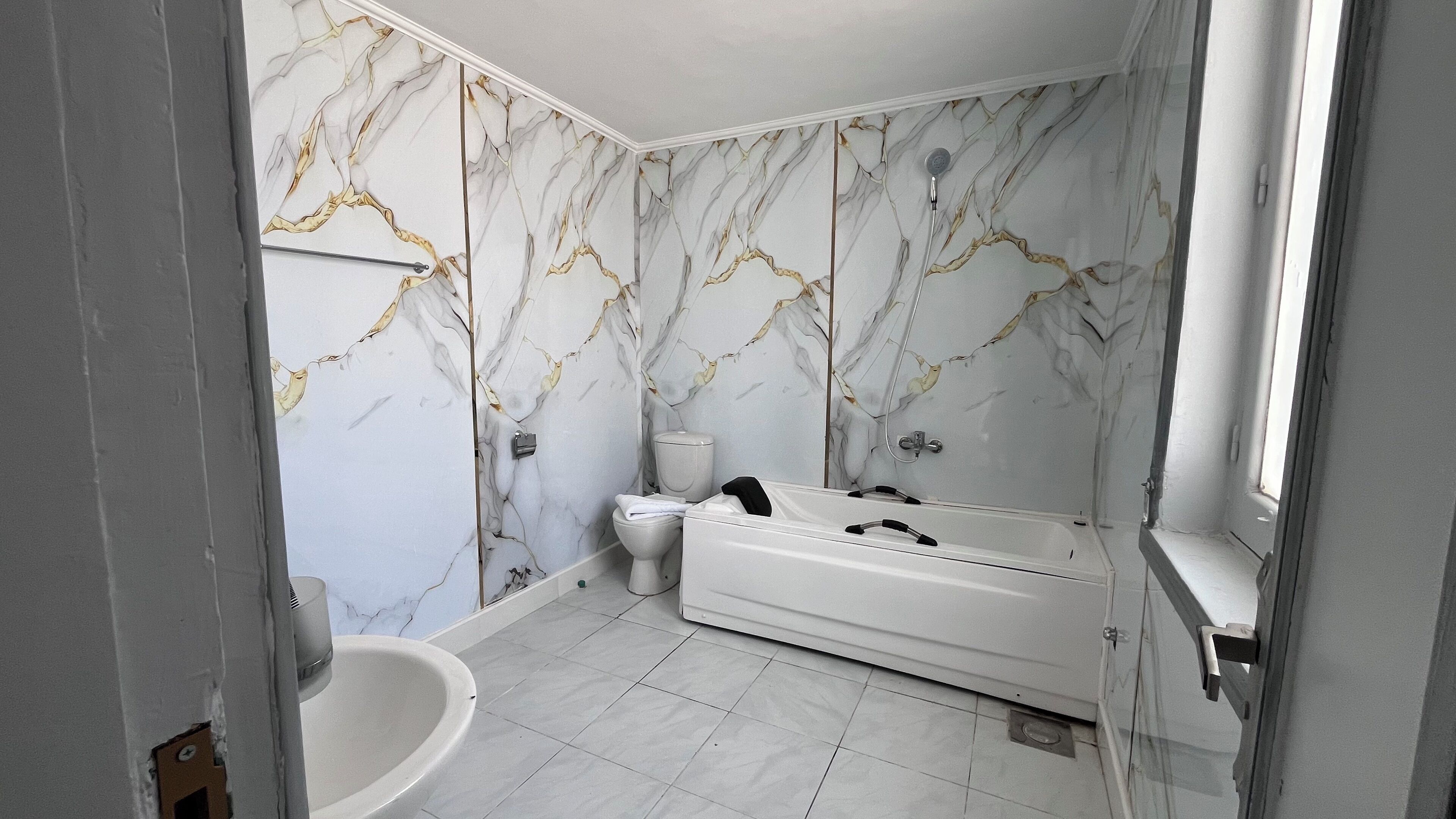 A bathroom with a bathtub, toilet, and sink, featuring marble-patterned walls.