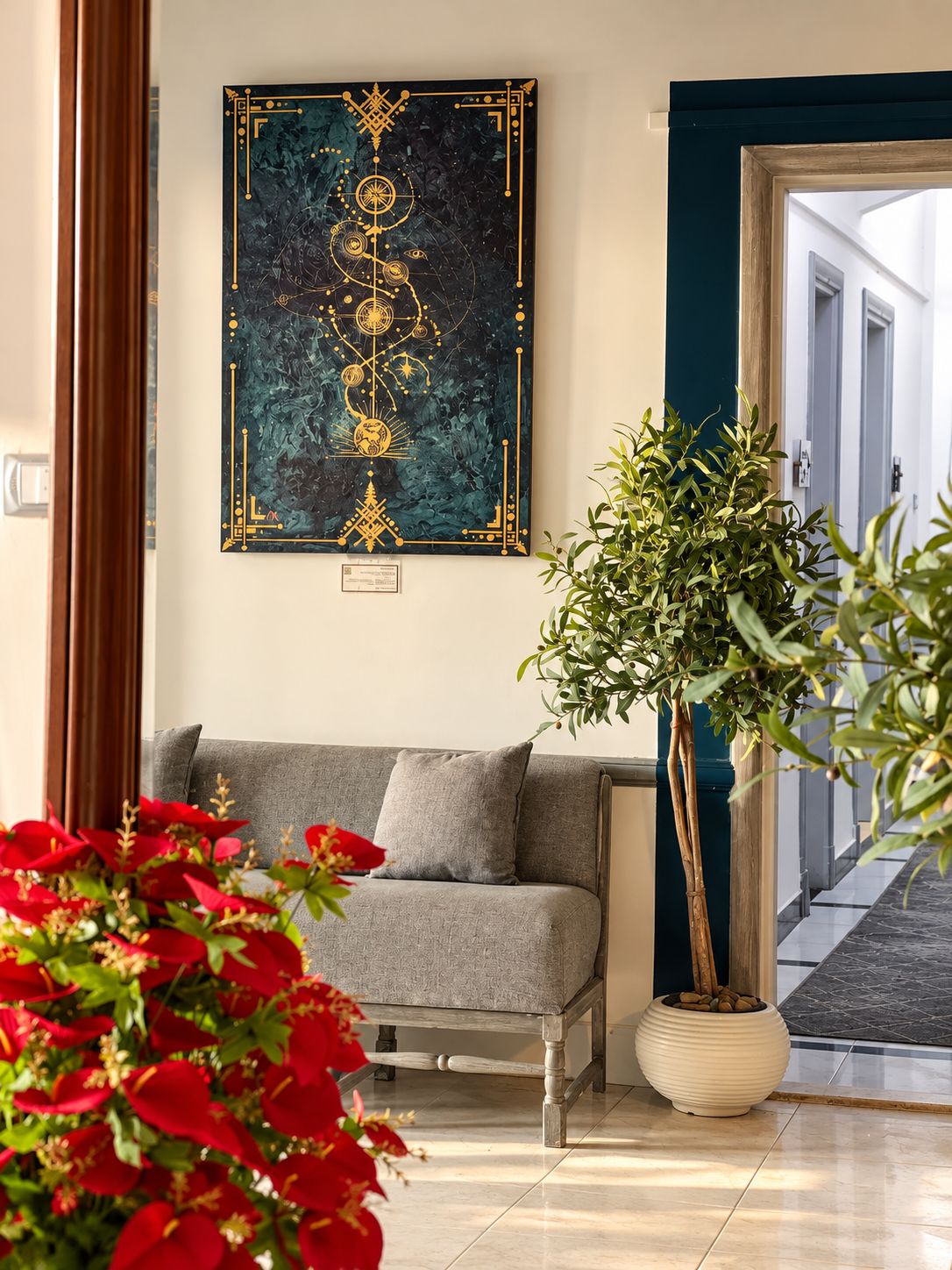 Una habitación con un sofá gris, un cuadro abstracto grande, una planta en maceta y flores rojas.