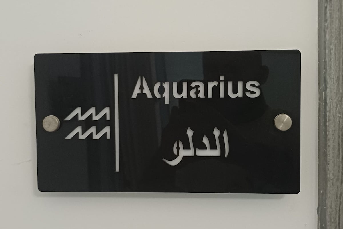 A black sign with 'Aquarius' and Arabic script on a white wall.