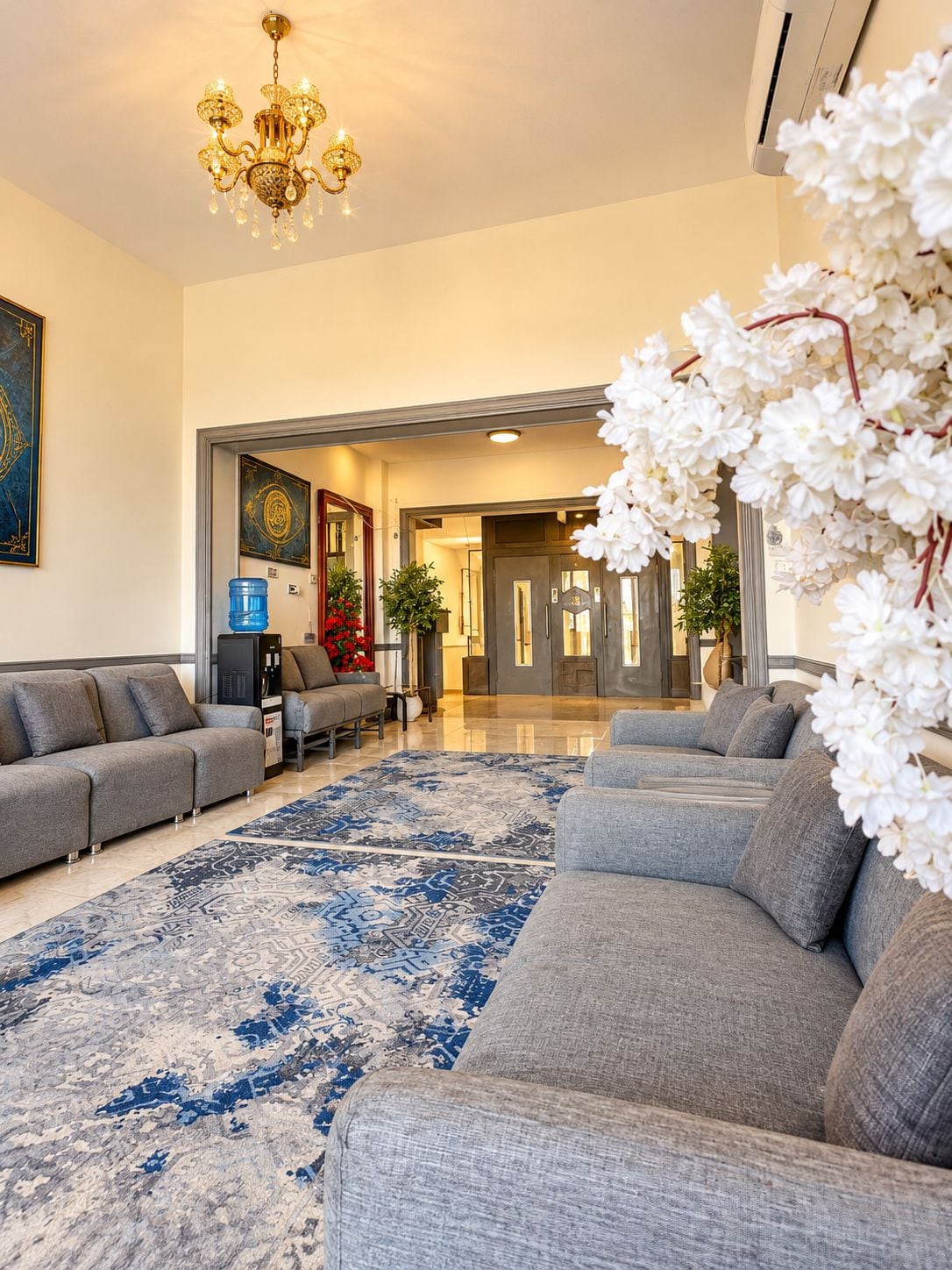 A modern living room with a grey sofa set, a patterned rug, and a chandelier.