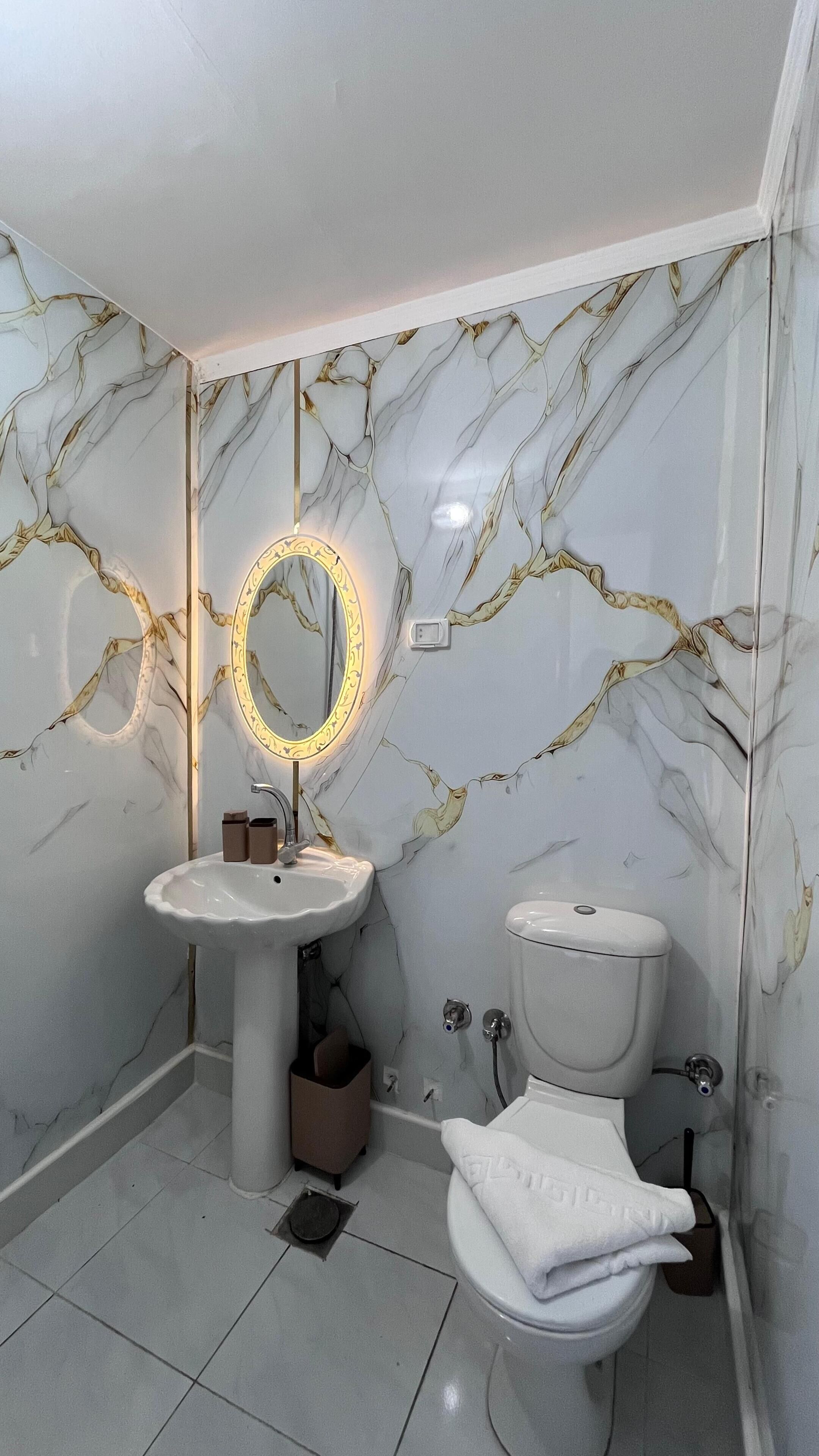 Ein Badezimmer mit Marmorwand, einem Standwaschbecken, einer Toilette und einem Schminkspiegel mit Beleuchtung.