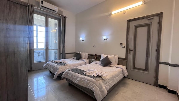 A hotel room with two beds, a door, a window with curtains, and wall-mounted lights. - Constellations Gateway Boutique Hotel (Cairo)