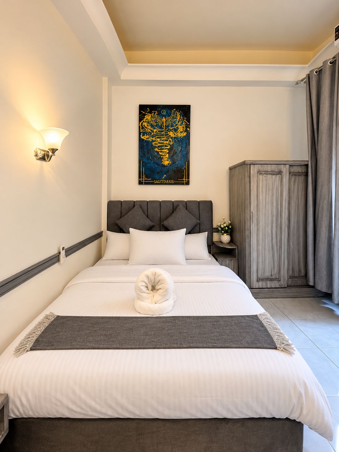 A neatly made bed with a white duvet, a grey throw blanket, and a decorative towel.