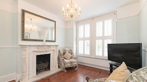 A room with a fireplace, a television, a chandelier, and large windows. - Spacious East London Home with a beautiful Garden - Pass the Keys (London)