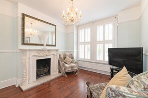 A room with a fireplace, a television, a chandelier, and large windows. - Spacious East London Home with a beautiful Garden - Pass the Keys (London)