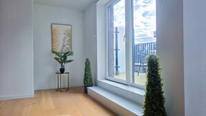 Una habitación con un ventanal grande, una planta en maceta, una mesita y un cuadro en la pared.