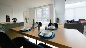 Un comedor moderno con una mesa de madera dispuesta para cuatro personas, sillas alrededor y vistas a un balcón y al paisaje urbano.