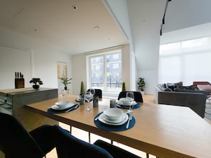 Ein moderner Essbereich mit Holztisch, gedeckt für vier Personen, umgeben von Stühlen, mit Blick auf einen Balkon und die Stadtlandschaft.