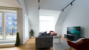 Un loft moderno con un ventanal grande, un sofá gris, una silla roja, un televisor y una planta pequeña.