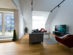 Eine moderne Loftwohnung mit großem Fenster, einem grauen Sofa, einem roten Sessel, einem Fernseher und einer kleinen Pflanze.