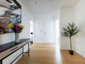 Ein Flur mit Holzboden, einer weißen Tür am Ende, einem schwarzen Konsolentisch mit Schubladen und einer Vase mit bunten Blumen.