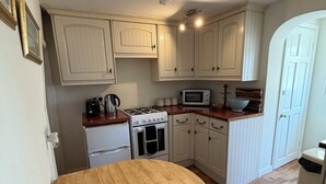 Une cuisine de taille réduite avec des meubles blancs, une cuisinière, un four à micro-ondes et un plan de travail en bois.