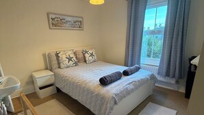 Une chambre à coucher comprenant un lit, des tables de chevet, une fenêtre avec des rideaux, un radiateur et un luminaire au plafond.