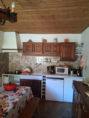 A compact kitchen with wooden cabinets, a microwave, a stove, and a dishwasher. - Authentic Vendée farmhouse set in a large wooded area 15 minutes from the sea (saint jean de monts)