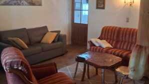 A living room with a wooden ceiling, a sofa, a striped armchair, a coffee table, and a painting on the wall. - Authentic Vendée farmhouse set in a large wooded area 15 minutes from the sea (saint jean de monts)
