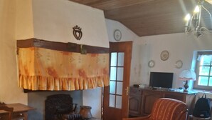 A cozy living room with a fireplace, a wooden ceiling, a patterned rug, and a comfortable armchair. - Authentic Vendée farmhouse set in a large wooded area 15 minutes from the sea (saint jean de monts)