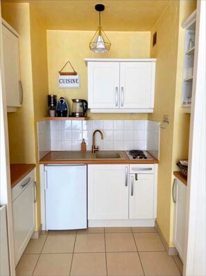 Eine kleine Küche mit weißen Schränken, einer Spüle, einer Kaffeemaschine und einem kleinen Kühlschrank.