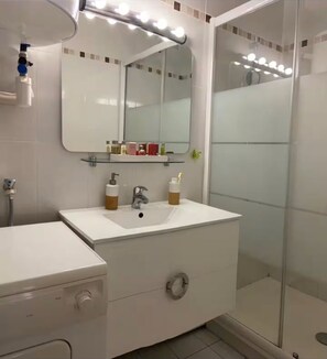 Ein Badezimmer mit weißem Waschtisch, einem Spiegel und einer Duschkabine aus Glas.