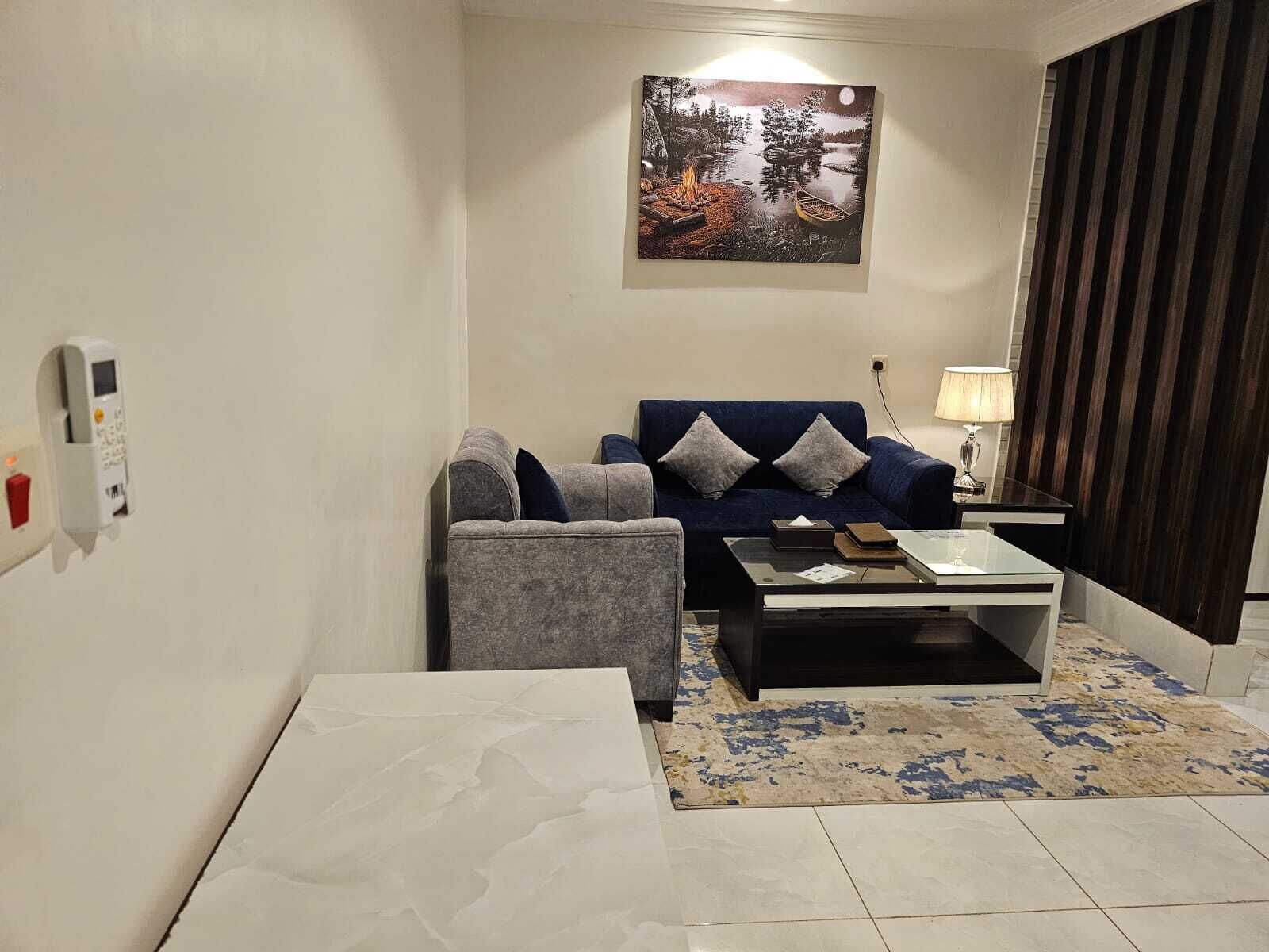 Una sala de estar con sofá, sillón, mesa de centro y un cuadro en la pared.